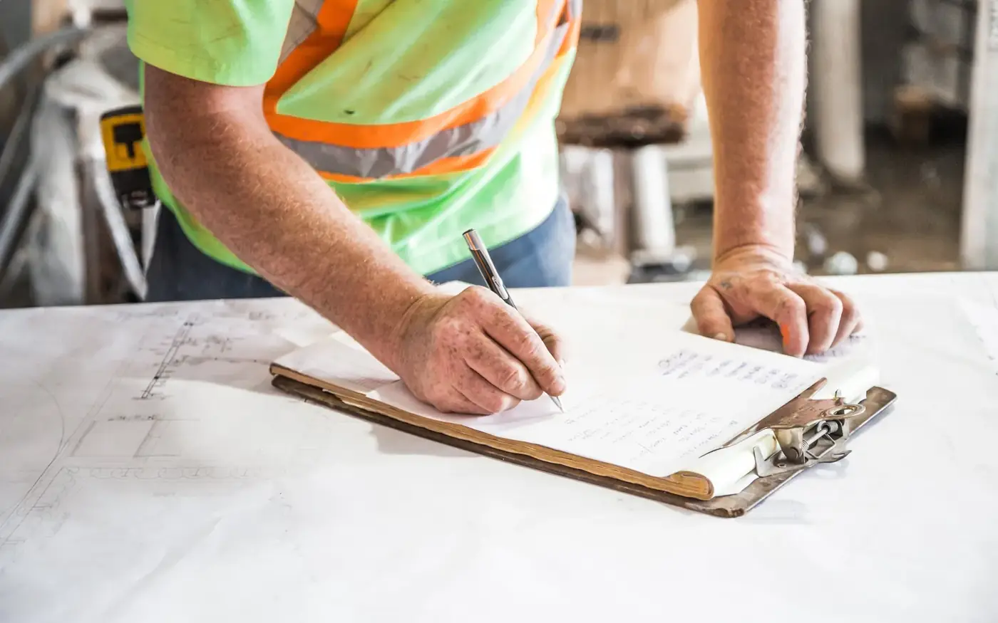 A worker in a hi-vis vest filling in a form on a clipboard at a building site